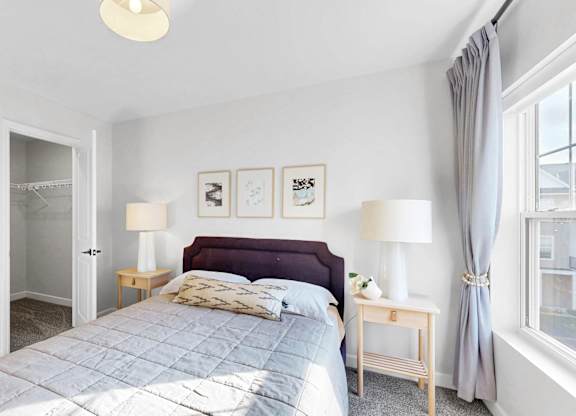 A bedroom with a large bed, two lamps, and a window with curtains.at Field and Grove Townhomes of Champlin, Champlin Minnesota