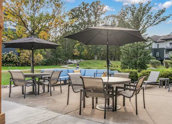 A patio with chairs and umbrellas is surrounded by trees and buildings.