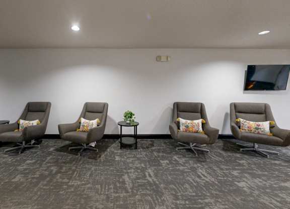 A row of grey chairs with cushions are lined up in a waiting room.