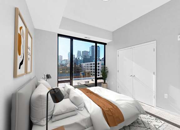 A bedroom with a large bed and a city view through the window.