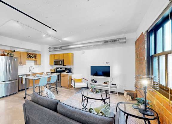 A modern living room with a grey couch and a kitchen in the background.