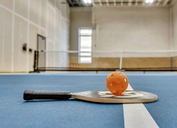 A small orange ball is on a paddle on a blue table.