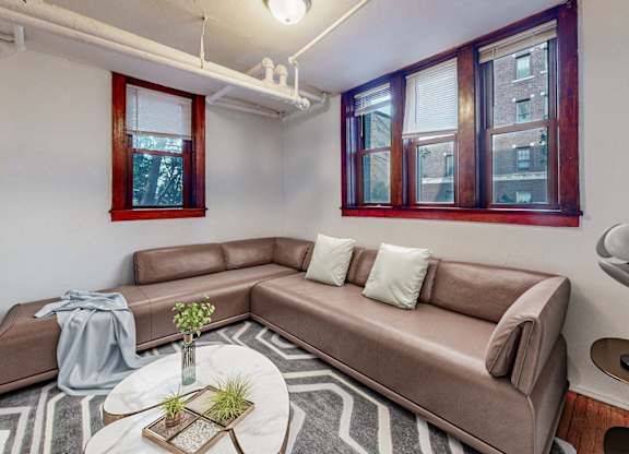 A living room with a brown couch, a small table with a vase and a plant, and a floor lamp.