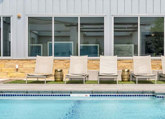 A pool with chairs and a building in the background.