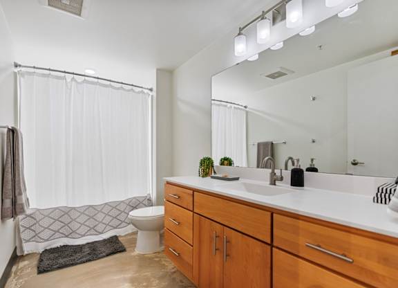 A bathroom with a white shower curtain and a black rug on the floor.