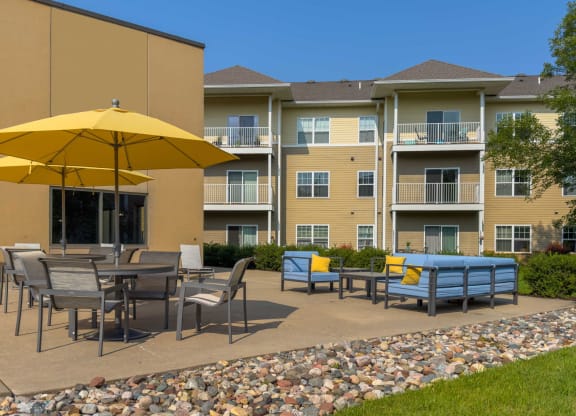 an outdoor patio with tables and umbrellas at chaska place apartments