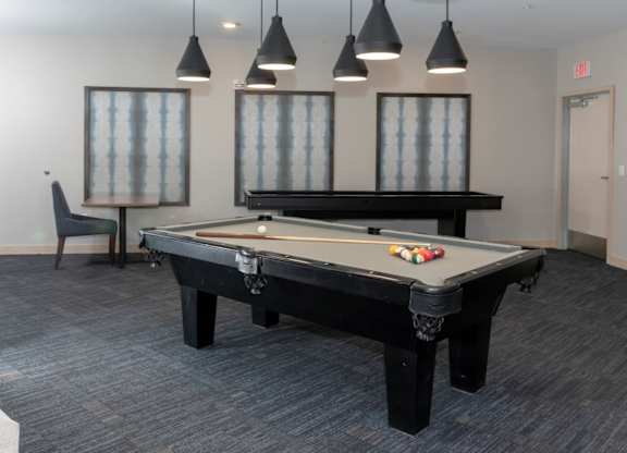 A pool table in a room with a chair and hanging lights.