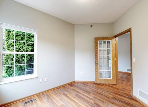 A room with a wooden floor, a window, and a door.