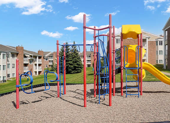A playground with a red and blue swing set, a yellow slide, and a red and blue jungle gym.
