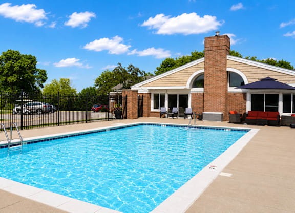 A swimming pool in front of a house with a black fence.