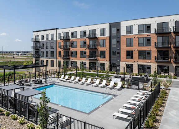 A pool surrounded by lounge chairs in front of apartment buildings.
