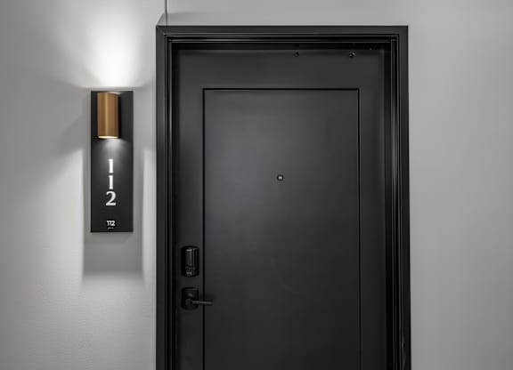 A black door with a gold handle and a sign above it that says 112.