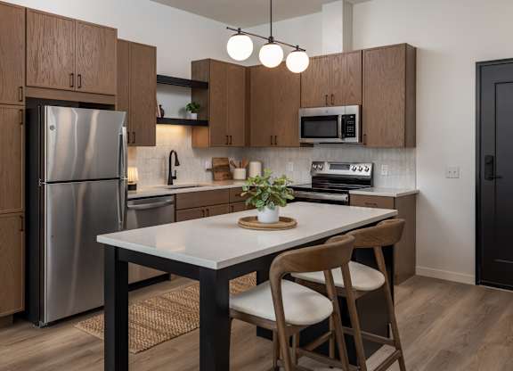 A kitchen with a table and chairs in the foreground and a refrigerator, microwave, and oven in the background.