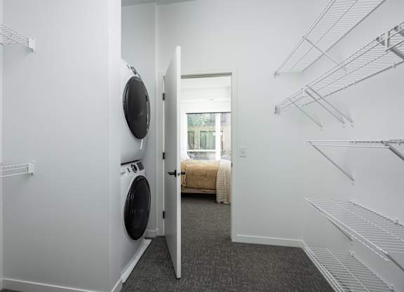 A laundry room with a washer and dryer and a doorway leading to a bedroom.