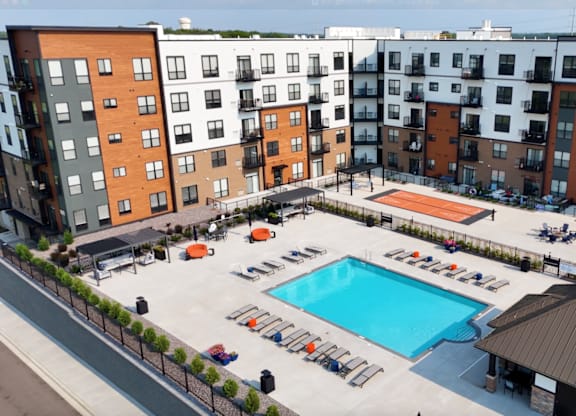 A large swimming pool surrounded by sun loungers and umbrellas in a courtyard surrounded by apartment buildings.