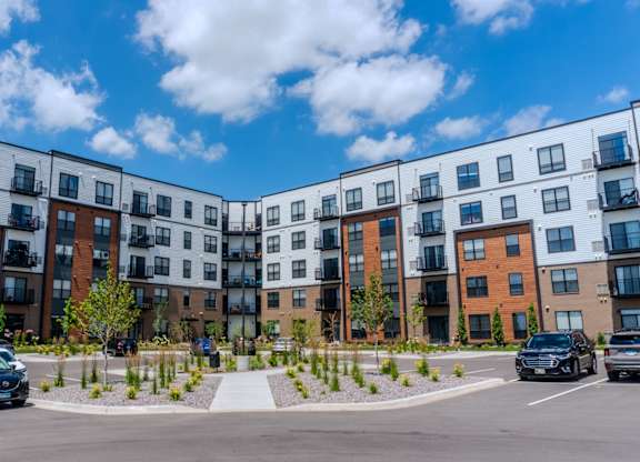 A row of modern apartment buildings with cars parked in front. at The Edison at Maple Grove, Maple Grove, MN, 55311