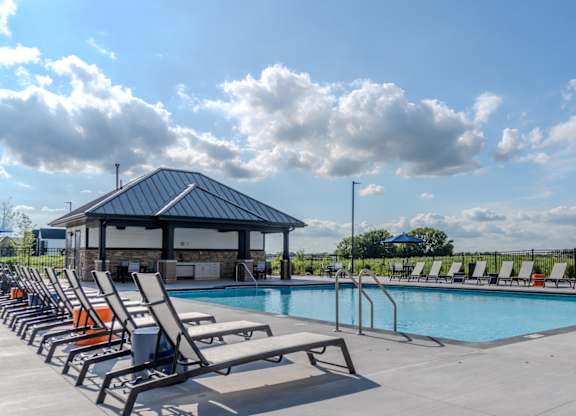 A pool with sun loungers and a pavilion is surrounded by a fence. at The Edison at Maple Grove, Minnesota, 55311