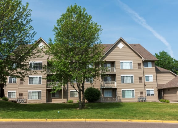 a large apartment building with tan siding and a large tree in front of it
