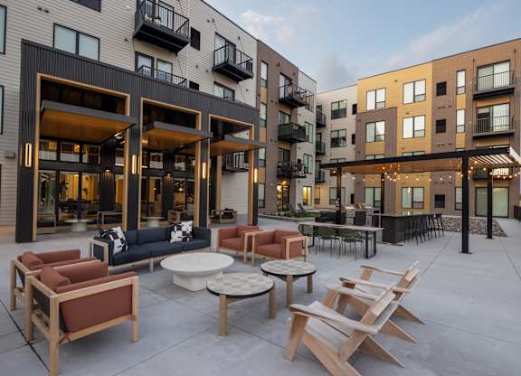 A patio with chairs and tables is surrounded by apartment buildings.