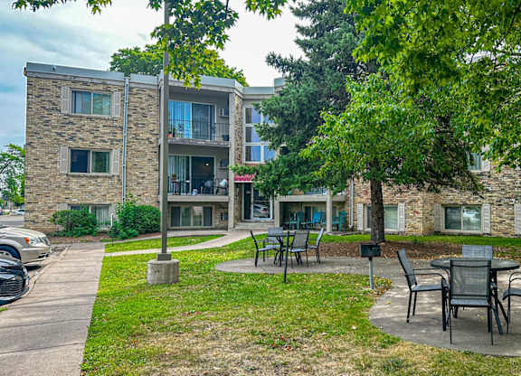 A patio with chairs and a table is surrounded by trees and apartment buildings.