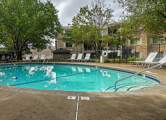 A large outdoor swimming pool surrounded by trees and lounge chairs.