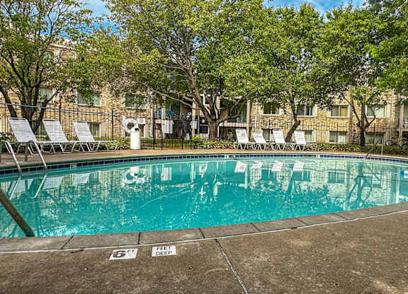 A large outdoor swimming pool surrounded by trees and chairs.