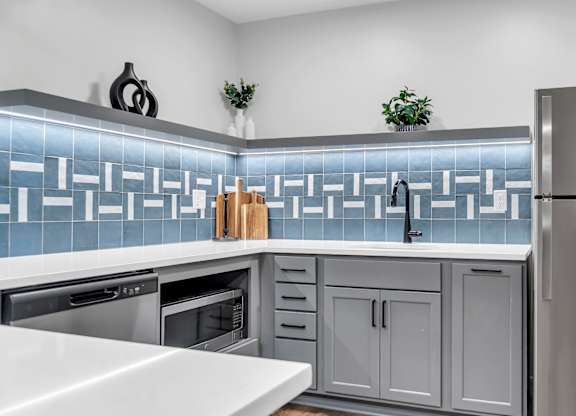 A modern kitchen with a stainless steel refrigerator and a backsplash of blue tiles. at Hillsborough Apartments, Minnesota