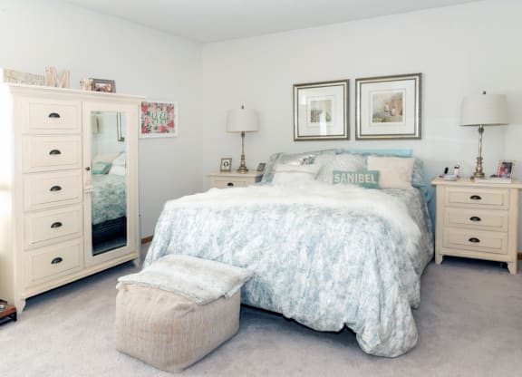 a bedroom with white walls and a bed with a white comforter and blue pillows