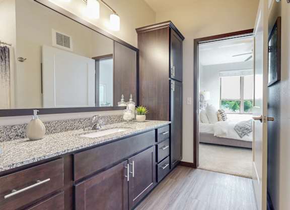A bathroom with a sink, mirror, and a large open door leading to a bedroom. at Lake Jonathan Flats, Chaska, Minnesota