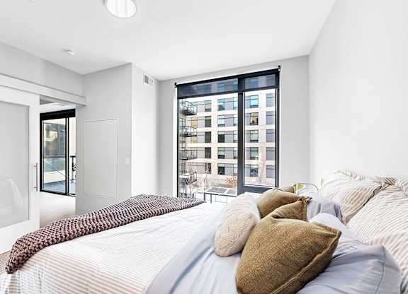 A bedroom with a large bed and a view of a cityscape through the window.