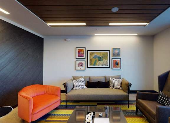 A living room with a grey couch, orange armchair, and a coffee table at The Bessemer at Seward Commons Apartments, Minnesota