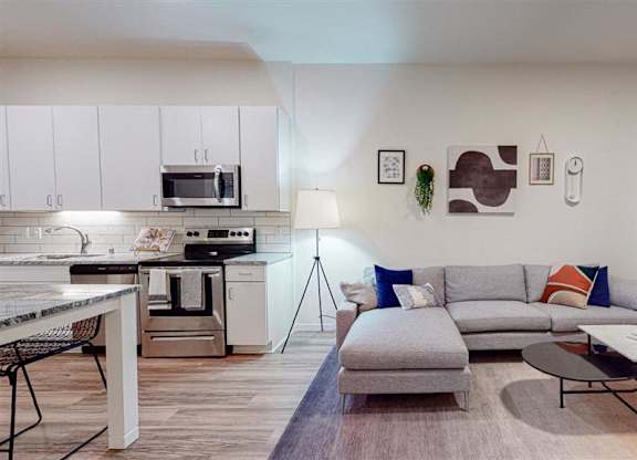 A modern kitchen with a grey sofa and a coffee table at The Bessemer at Seward Commons Apartments, Minneapolis, MN,  55404
