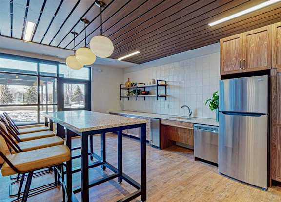 A kitchen with wooden cabinets and a stainless steel refrigerator at The Bessemer at Seward Commons Apartments, Minnesota