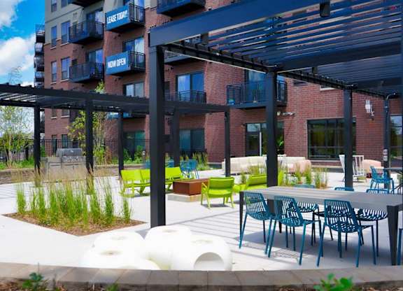 A patio area with tables and chairs is surrounded by a building at The Bessemer at Seward Commons Apartments, MN, 55404