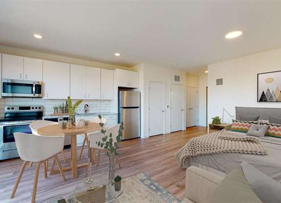 A modern kitchen with a dining table and a bedroom with a bed at The Bessemer at Seward Commons Apartments, Minnesota, 55404