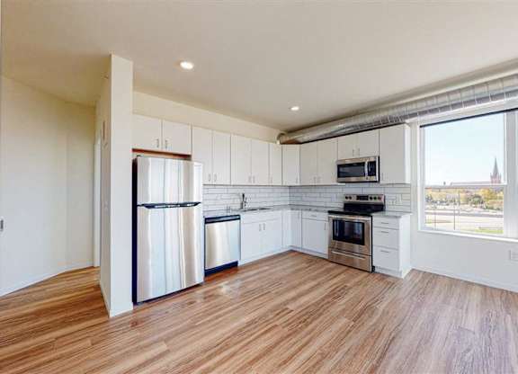 A kitchen with white cabinets and a wooden floor at The Bessemer at Seward Commons Apartments, Minnesota