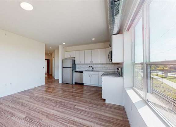 A kitchen with white cabinets and a refrigerator is shown at The Bessemer at Seward Commons Apartments, MN, 55404