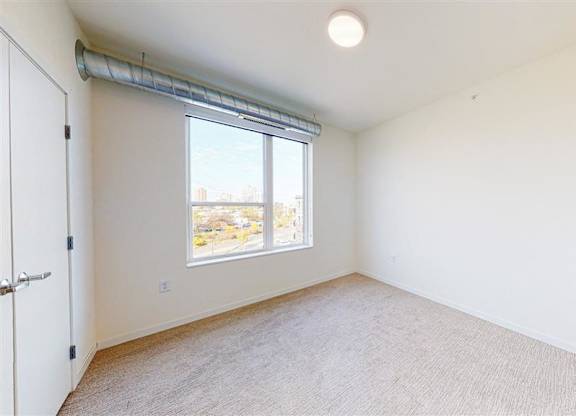 A room with a carpeted floor and a window with blinds at The Bessemer at Seward Commons Apartments, Minneapolis