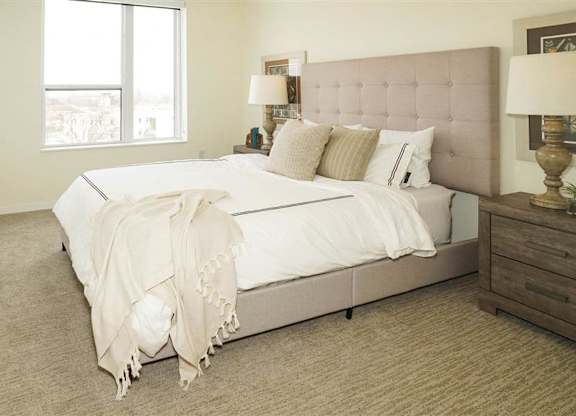A bedroom with a large bed and a lamp on the side table at The Bessemer at Seward Commons Apartments, Minneapolis, Minnesota