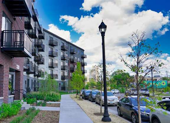 A street view of a residential area with cars parked on the side of the road at The Bessemer at Seward Commons Apartments, Minnesota
