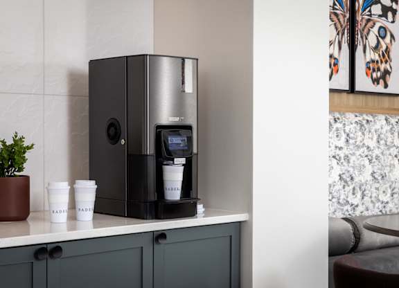 A coffee machine is on a counter with two cups labeled