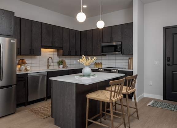 A kitchen with a refrigerator, sink, and bar stools.
