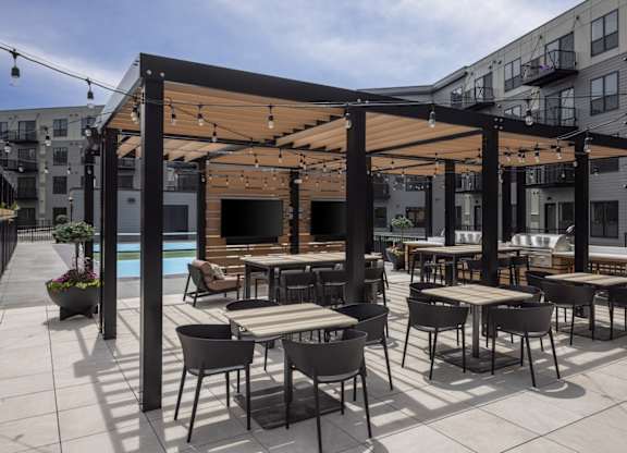 A patio with tables and chairs and a pool in the background.