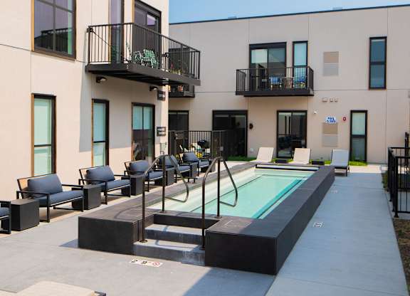 A modern building with a pool and lounge chairs.