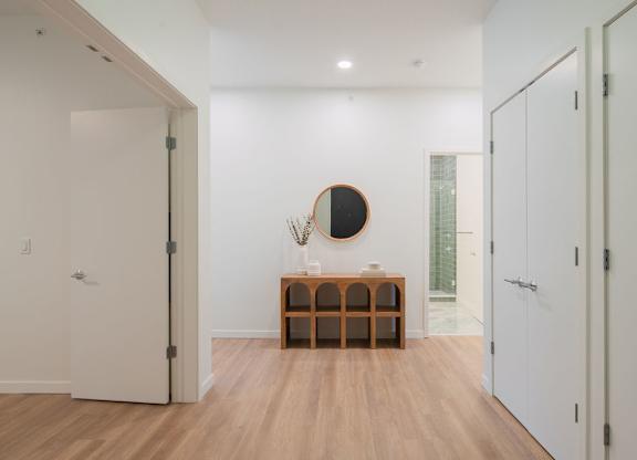 A white hallway with a round mirror and a wooden bench.
