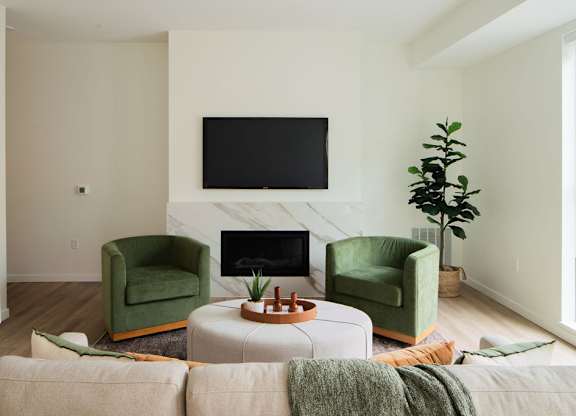 A living room with a fireplace, two green chairs, and a television.