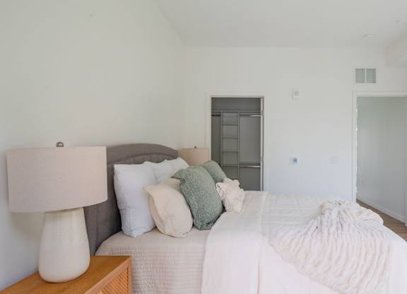 A white bedroom with a large bed and a lamp on the nightstand.