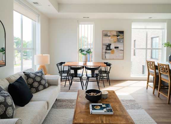 A modern living room with a white couch, a wooden coffee table, and a dining table with chairs.
