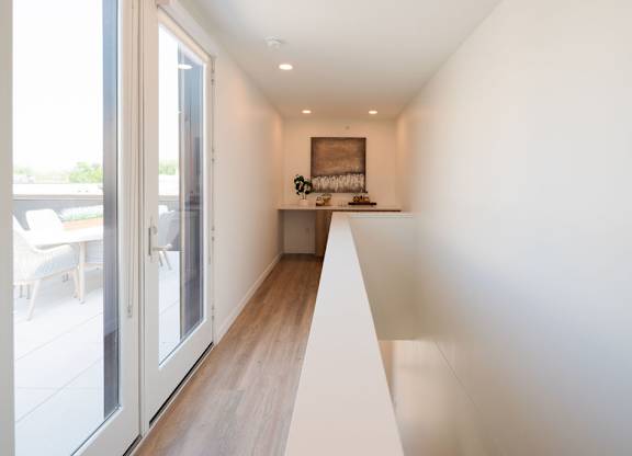 A long white hallway with a shelf and a picture on the wall.
