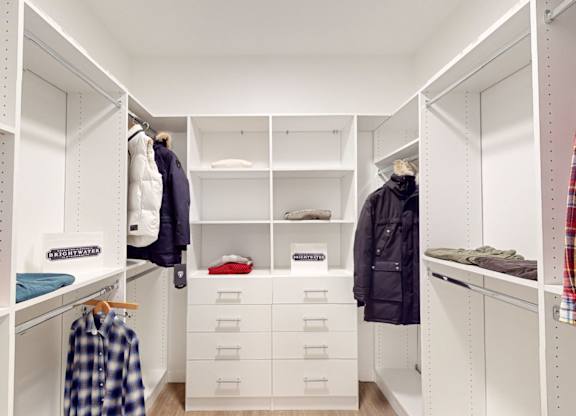 A white closet with clothes hanging and drawers underneath at One West Drive Apartments, Excelsior